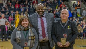 A group of 3 people smiling toward the camera at a sporting event.