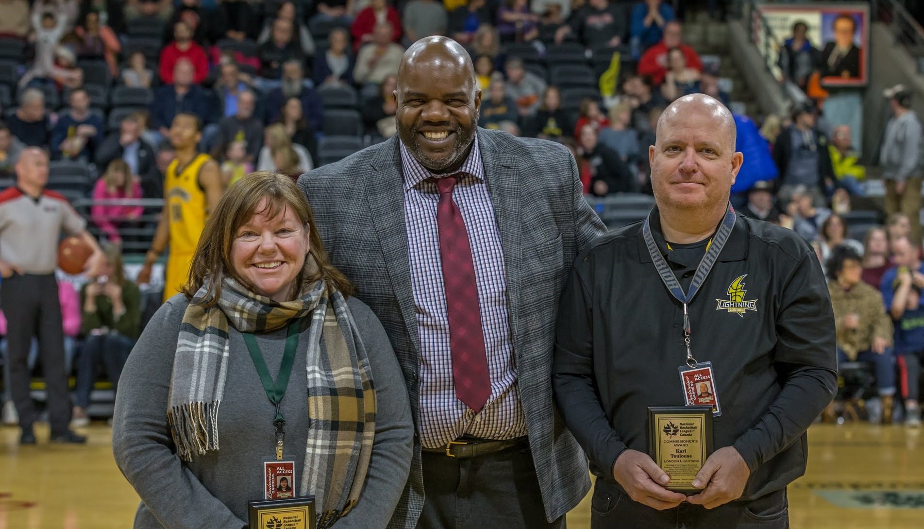 A group of 3 people smiling toward the camera at a sporting event.